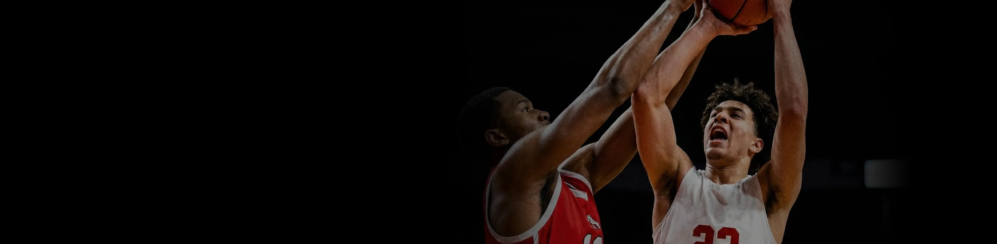 Two basketball players in red and white jerseys jumping to catch the ball.